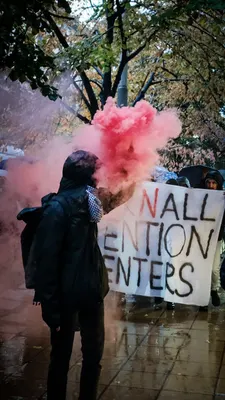 Protesters with red smoke flares march behind a banner against detention centers